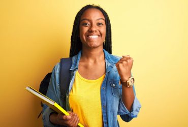 African american student woman wearing backpack and book over isolated yellow background screaming proud and celebrating victory and success very excited, cheering emotion